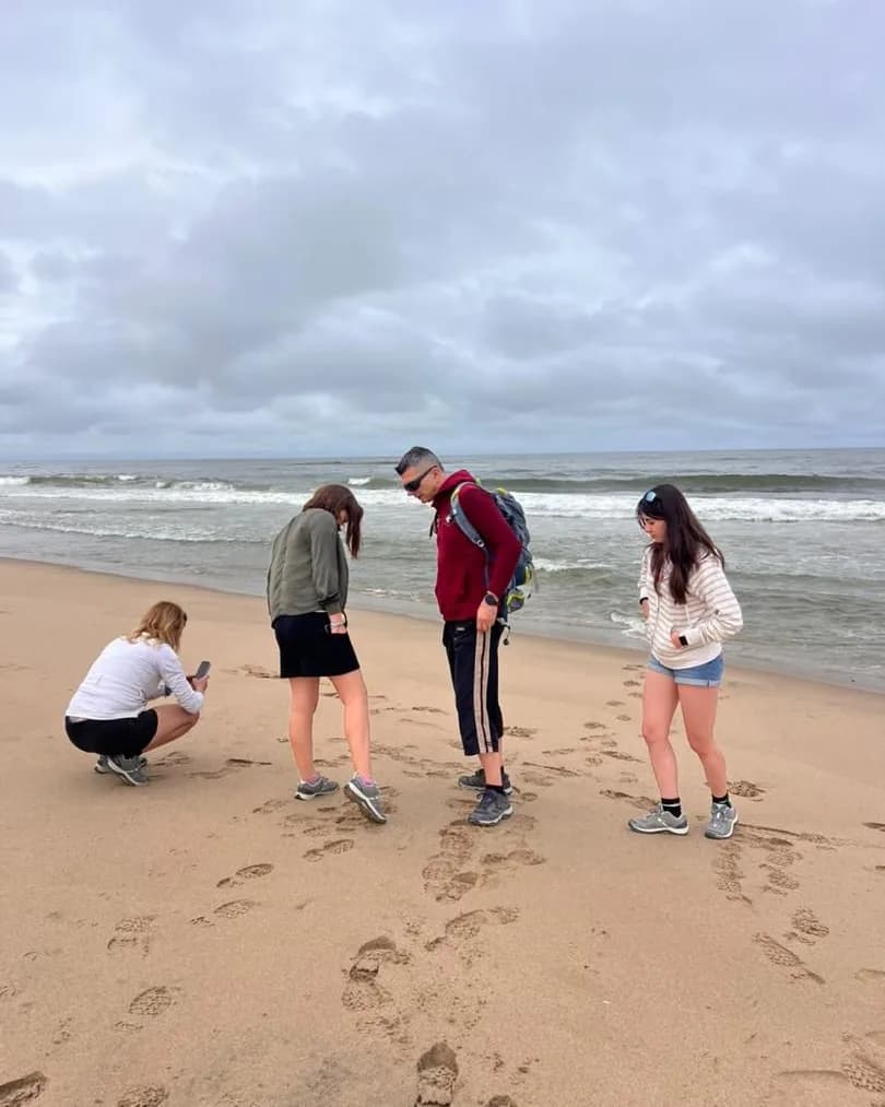 Vier Gäste auf einem weiten Atlantikstrand, eine Person hockt, um Abdrücke im Sand zu fotografieren