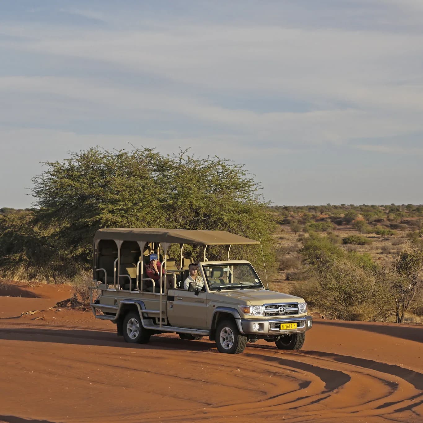 Oop safari voertuig met twee gaste wat oor rooi sand by goue ure ry