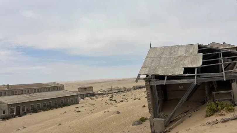 Verweerde houtgeboue wat stadig deur vorderende woesty sand begrawe word