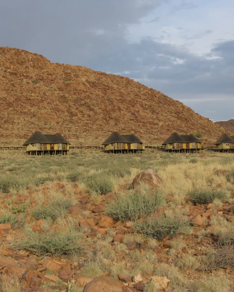 Ry van rietdak chalets op palings onder ’n rooi rotshelling