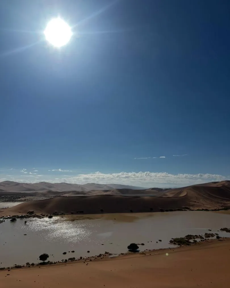 Die Sonne bricht über Dünen hervor, über einer dünnen Wasserschicht auf dem Sand